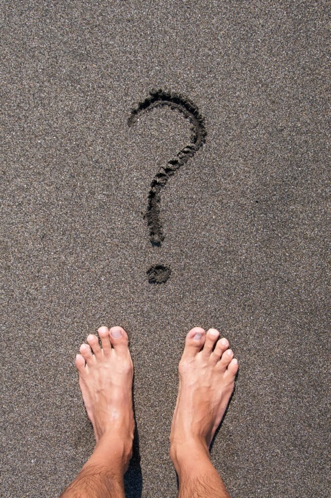 Bare feet on sandy beach with question mark in sand, symbolizing contemplation in Bali.